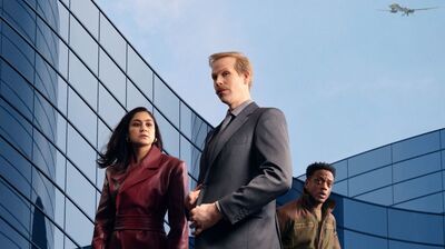 Drie professionals in formele kleding lopen langs moderne glazen gebouwen. De sfeer is zakelijk en dynamisch.