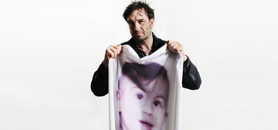 Man houdt een groot doek omhoog met een afbeelding van een kind. Achtergrond is wit.