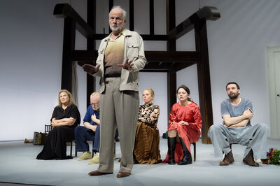 Een acteur staat op het podium voor een groep zittende mensen in een theatervoorstelling.