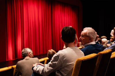 Theaterbezoekers wachten voor een rood voordoek tot de start van een voorstelling in de Pleinzaal