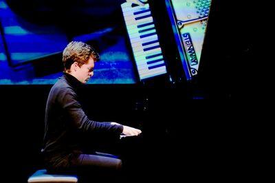 Een jonge man speelt piano op een podium, met een achtergrond van pianoklokken en kleurenlicht.