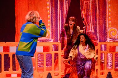 Meisje, hoofdpersoon Rosa, uit Hoe overleef ik alles wat ik niemand vertel - de musical, maakt foto van haar twee vriendinnen tussen een gordijn.