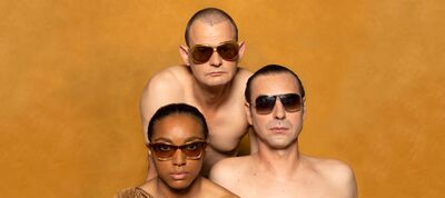 Drie mensen met zonnebrillen poseren topless tegen een oranje achtergrond.