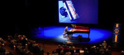 Een pianist speelt op een vleugelpiano op een podium voor een publiek in een theater.