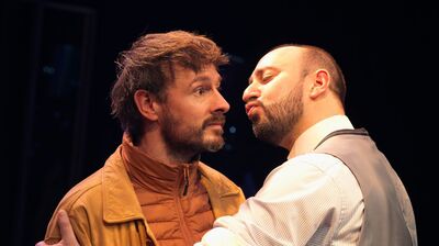 Twee mannen in een intense interactie op een podium, één kijkt verbijsterd, de ander benadert hem.