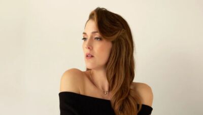 Portret van een vrouw met schouderlange, golvende haren, gekleed in een zwarte off-shoulder top, met een serene blik.