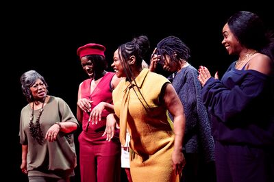 Groep vrouwen op een podium, elk in verschillende outfits, met lachende gezichten en enthousiaste lichaamstaal.