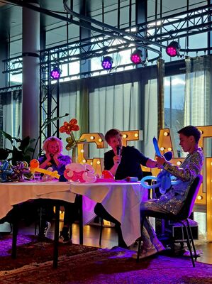 Drie mensen zitten aan tafel met decoratieve verlichting, bezig met een interactief evenement of presentatie.