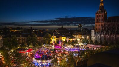 Luchtfoto van een levendig nachtelijk festival met kleurrijke lichtjes en attracties in een stadsplein.